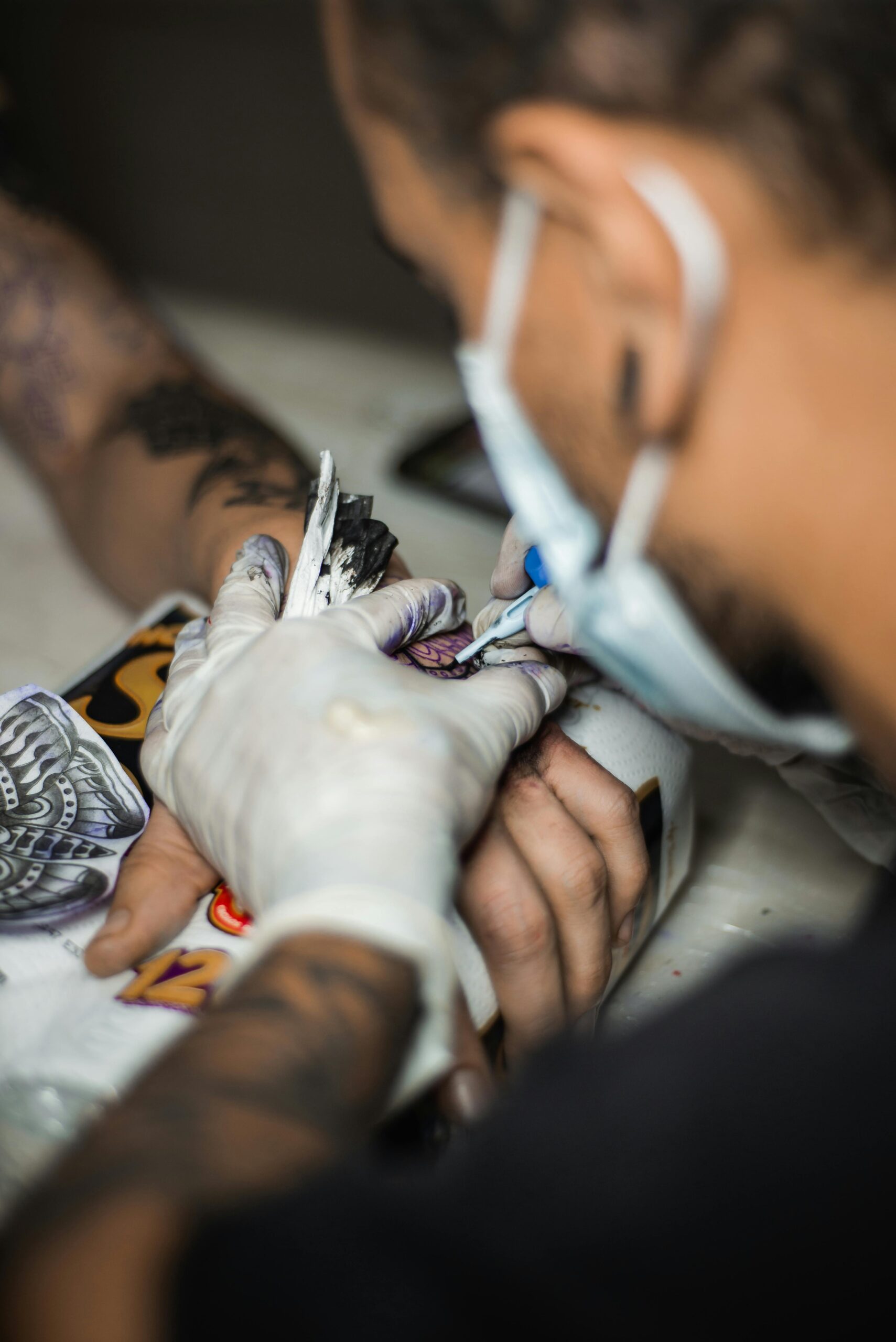 Tattoo artist wearing gloves working on a detailed hand tattoo using a cartridge needle
